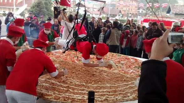 Um pizzaiolo precisou ser suspenso sobre a pizza para alcançar o meio da massa gigante e colocar o recheio / Foto: RankBrasil