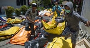 Familiares carregam corpo de vítima do terremoto em Palu, na região central da Indonésia, em meio a vários cadáveres espalhados (Foto: Bay Ismoyo/AFP)