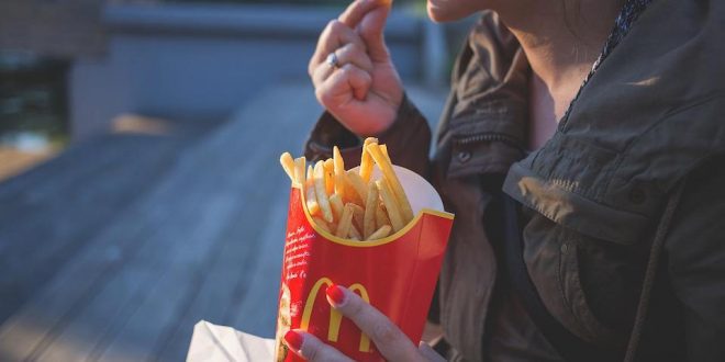 Mulher comendo batata frita de rede de fast food