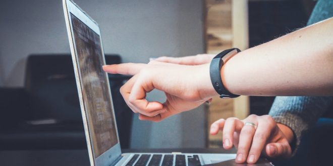Mão aponta para tela de notebook enquanto outra move o cursor do teclado