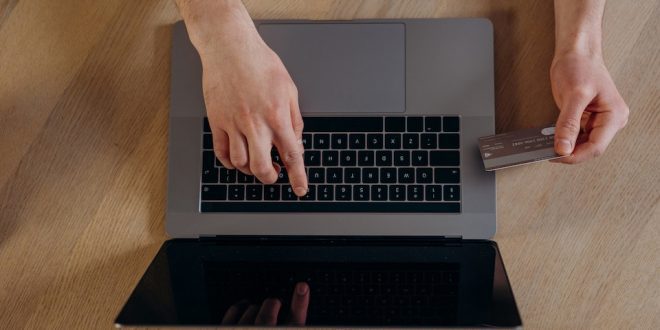 Pessoa mexe no computador com cartão de crédito na mão