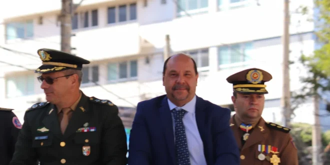 Prefeito Guilherme Guimarães passando revista às tropas e saudando a bandeira nacional, acompanhado por representantes das forças de segurança