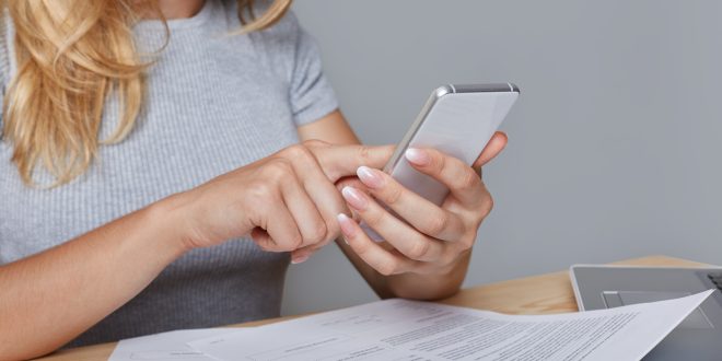 unrecognizable woman holds modern mobile phone hands sits work table surrounded with documents laptop pencil calculator downloads necessary information from internet job technology