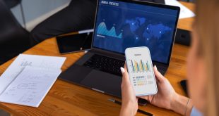 Uma pessoa usando notebook e celular enquanto analisa gráficos financeiros